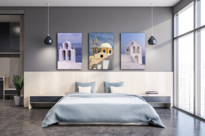 Three image set of beautiful churches in Santorini Greece displayed above the bed in the bedroom of a modern apartment.
