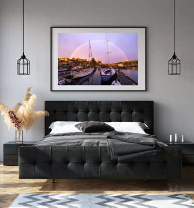 large framed fine art print of sailboats under a rainbow displayed above a bed in a modern home
