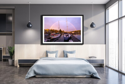 Large framed print of sailboats under a rainbow in Friday Harbor displayed above a bed in a modern apartment