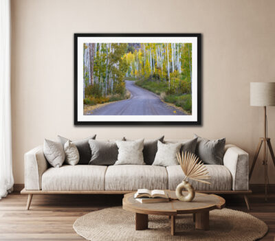large framed fine art print of a mountain road during fall displayed above the couch of a modern home