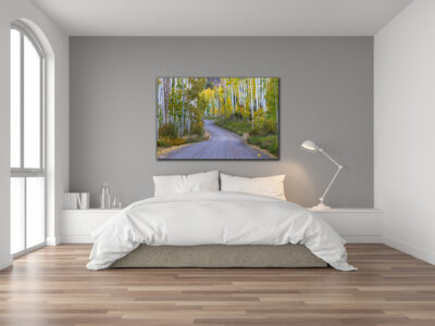 Large unframed fine art print of a winding mountain road during fall colors displayed above the bed in a modern home