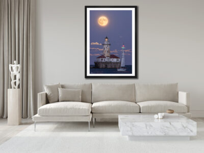 large fine art framed print of a super moon rising behind Chicago's Navy Pier lighthouse with a sailboat crossing in front displayed in the living room of a luxury modern home