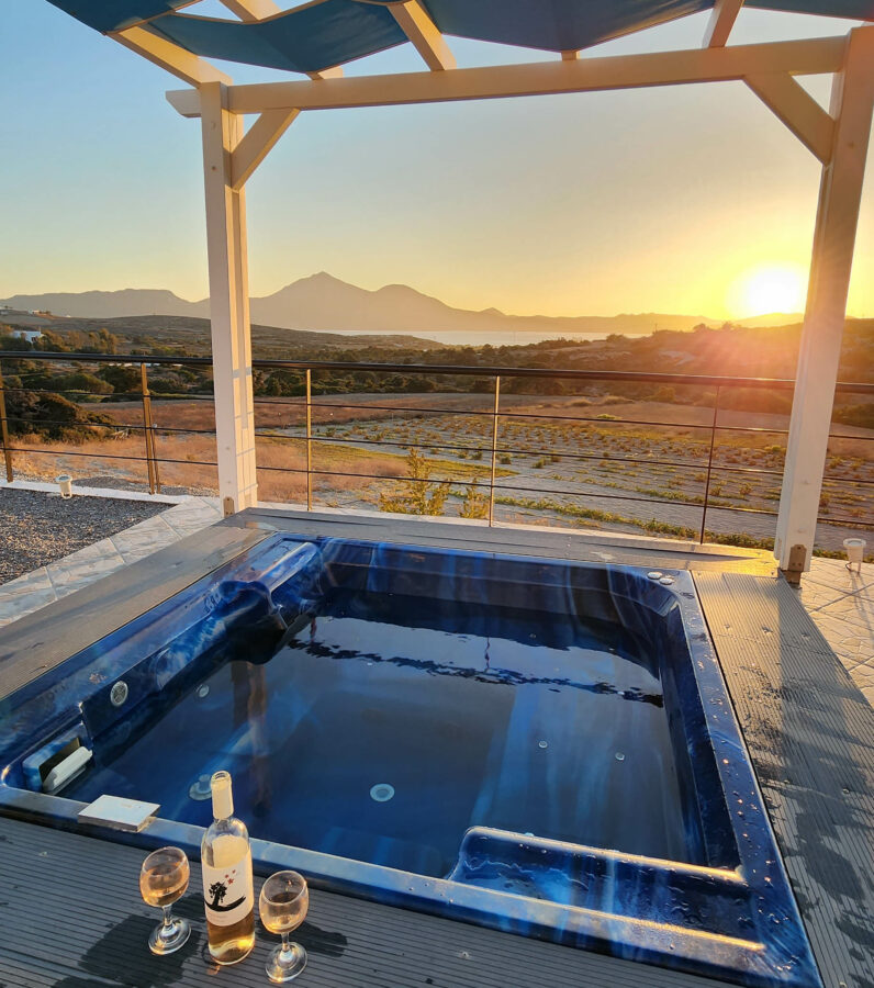 image of a hot tub on Milos Island in Greece with a bottle of wine looking at a beautiful sunset by the mountains 