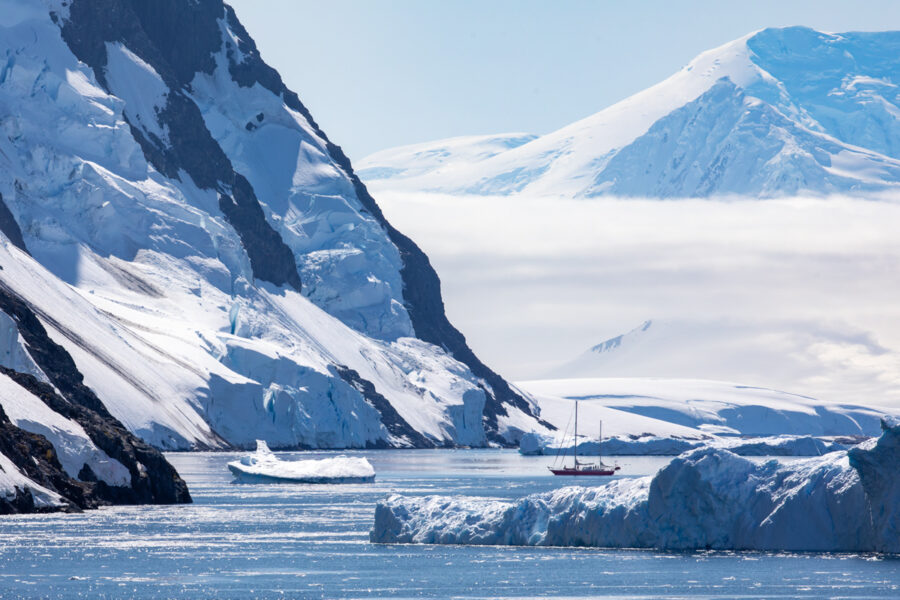 Photograph of a sailboat in Antarctica sailing through the tall mountains