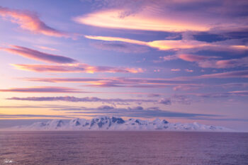 Image of Antarctica during a sunset with pink clouds over the snow covered mountains