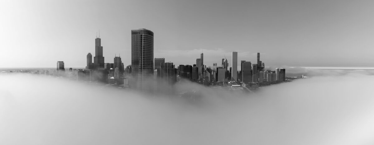 Black and white panoramic photo of Chicago surrouded by fog with only the skyscrapers sticking out above the clouds