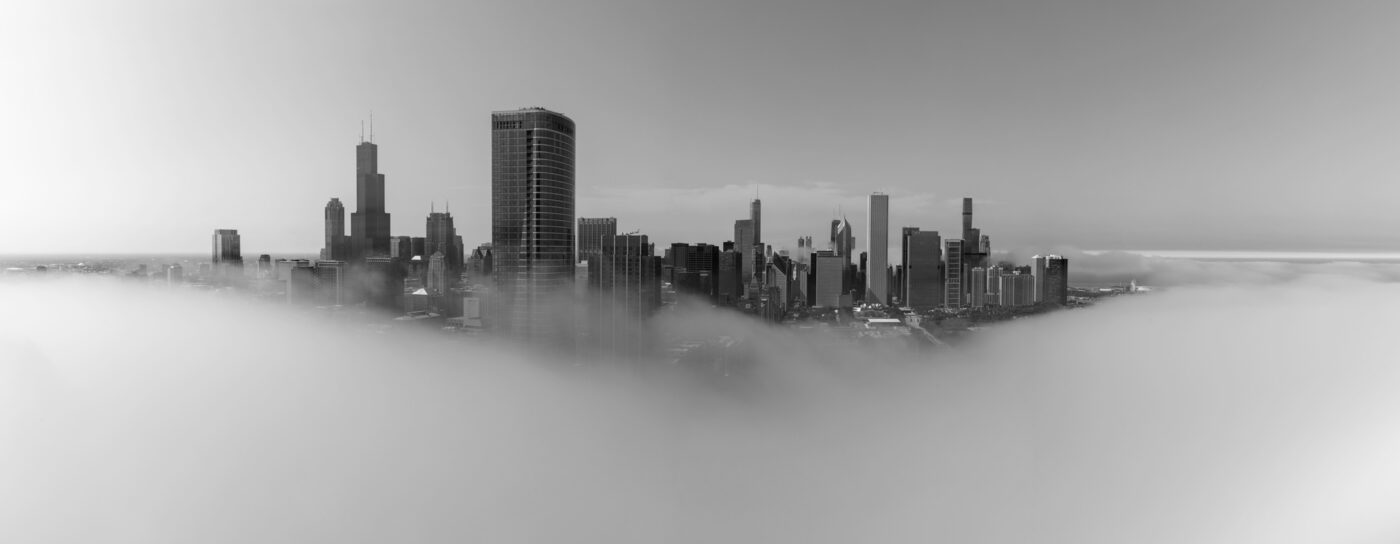 Black and white panoramic photo of Chicago surrouded by fog with only the skyscrapers sticking out above the clouds