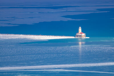 photograph of a blue light lake with ice in it and a solo lighhouse in the light