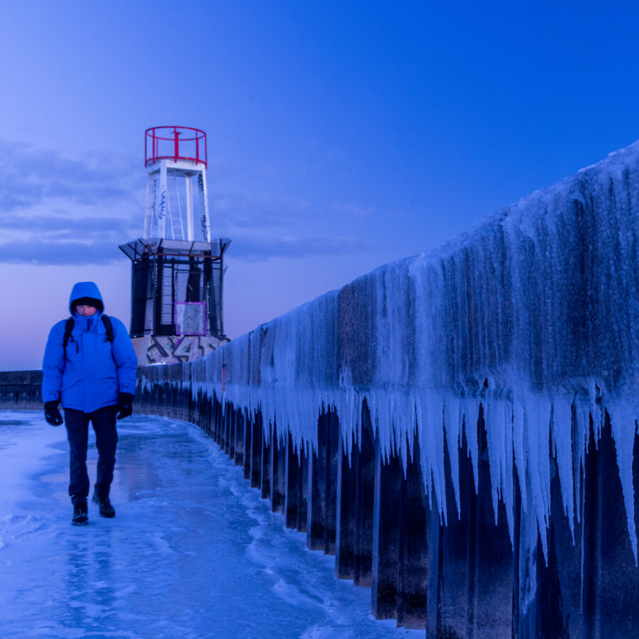 Photographer Derek Nielsen walking along a frozen wall in Chicago's winter